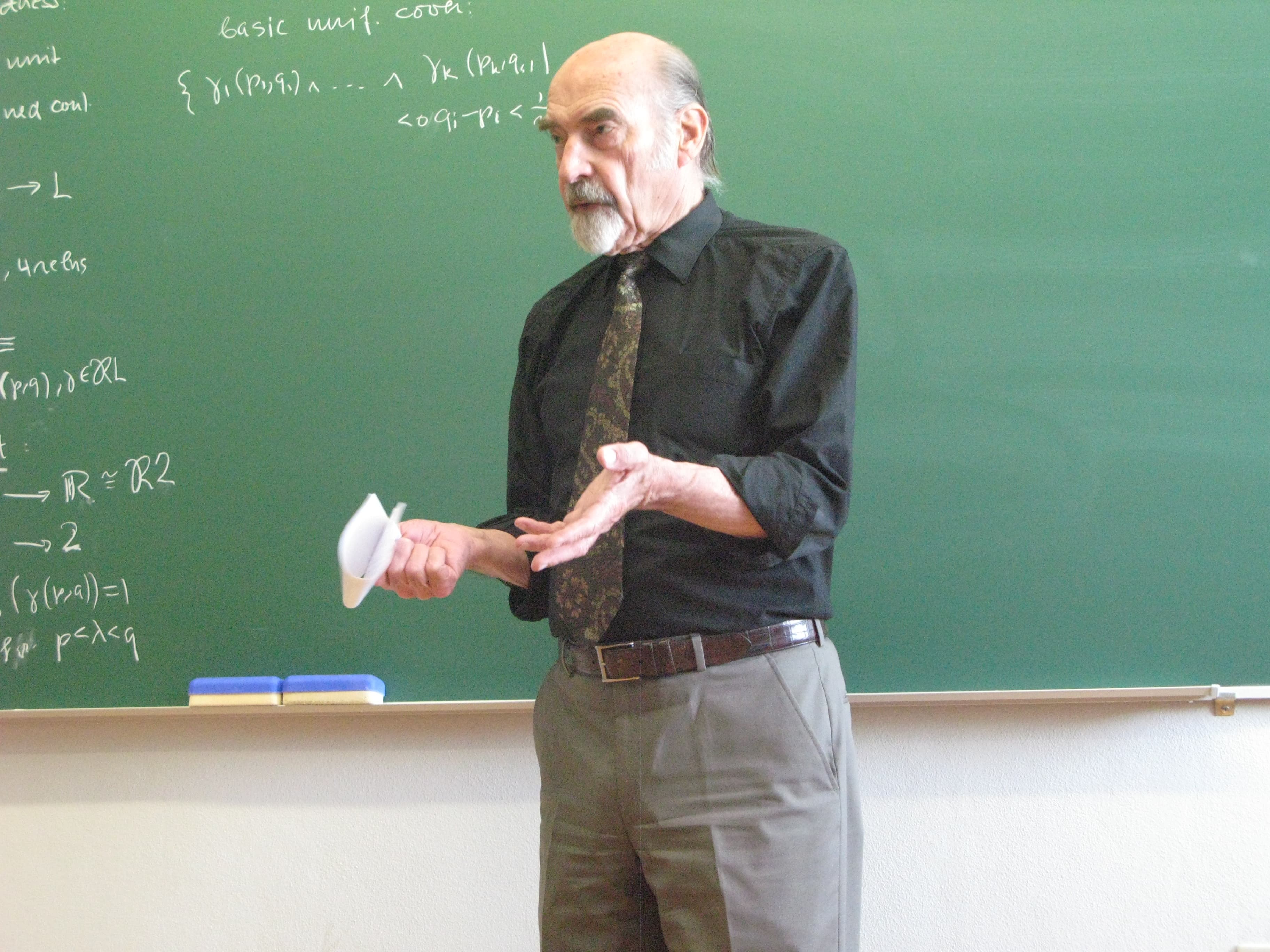 Bernhard Banaschewski lecturing in front of a green chalkboard covered in notation