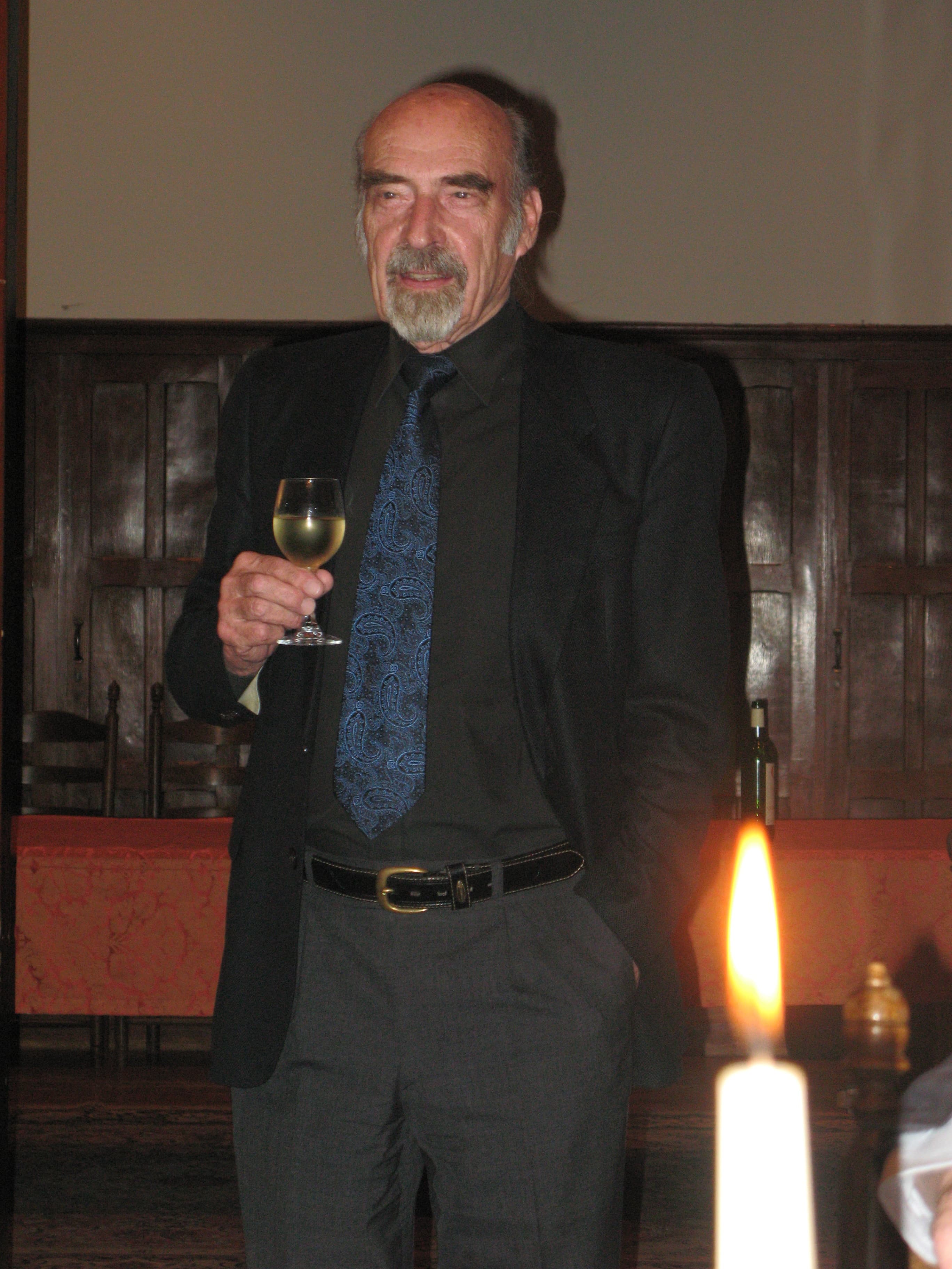 Bernhard Banaschewski standing with a glass of white wine raised, a candle in the foreground
